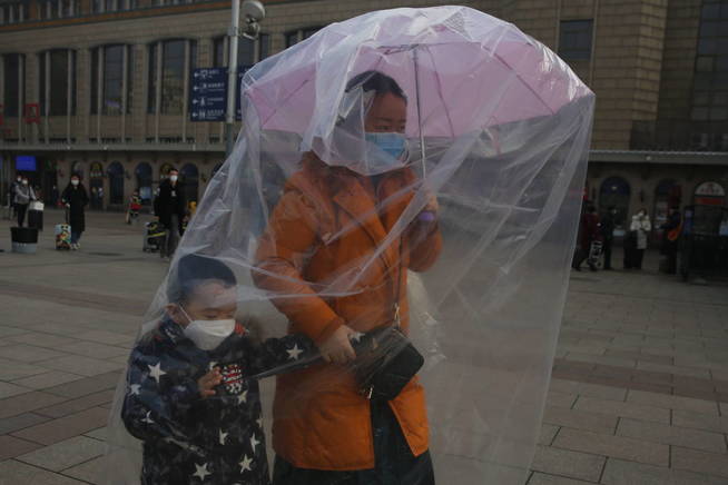 beijing-china-11-02-2020-a-passenger-wearing-protective-mask-and-holding-an-umbrella-to-hang-plastic-bags-to-cover-herself-and-her-chid-s-body-as-protection-from-coronavirus-at-beijing